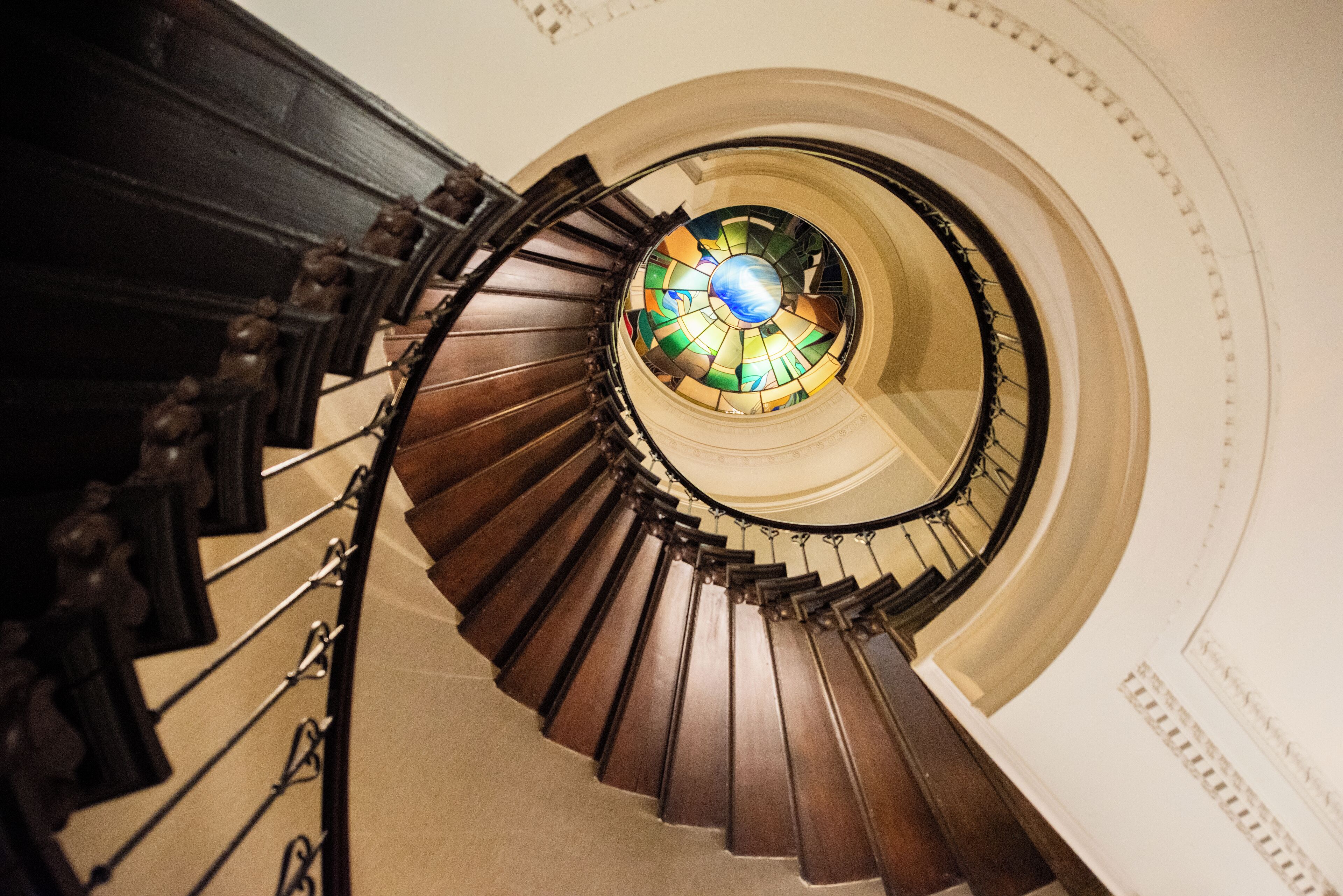 Un escalier en colimaçon surmonté d’une fenêtre à vitraux.