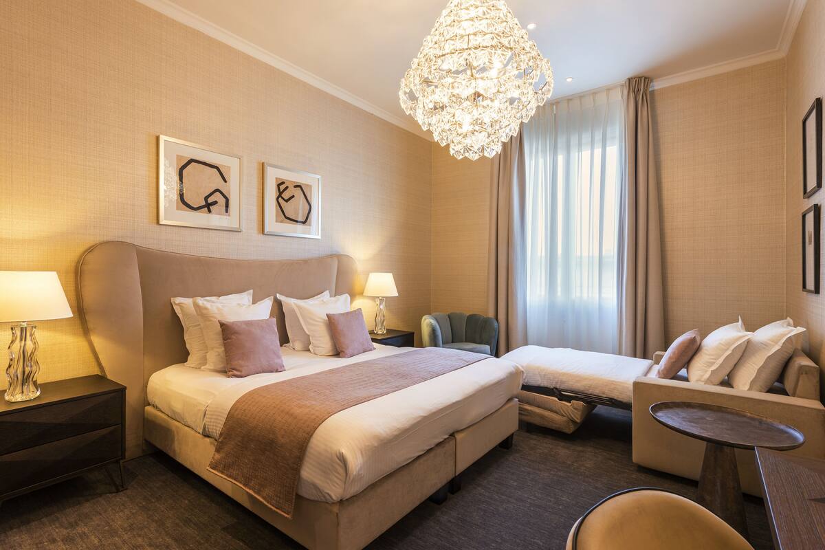 Ein Hotelzimmer mit einem großen Bett, einem Einzelbett, einem Schlafsofa, einem Sessel, einem Tisch und einer Deckenleuchte.