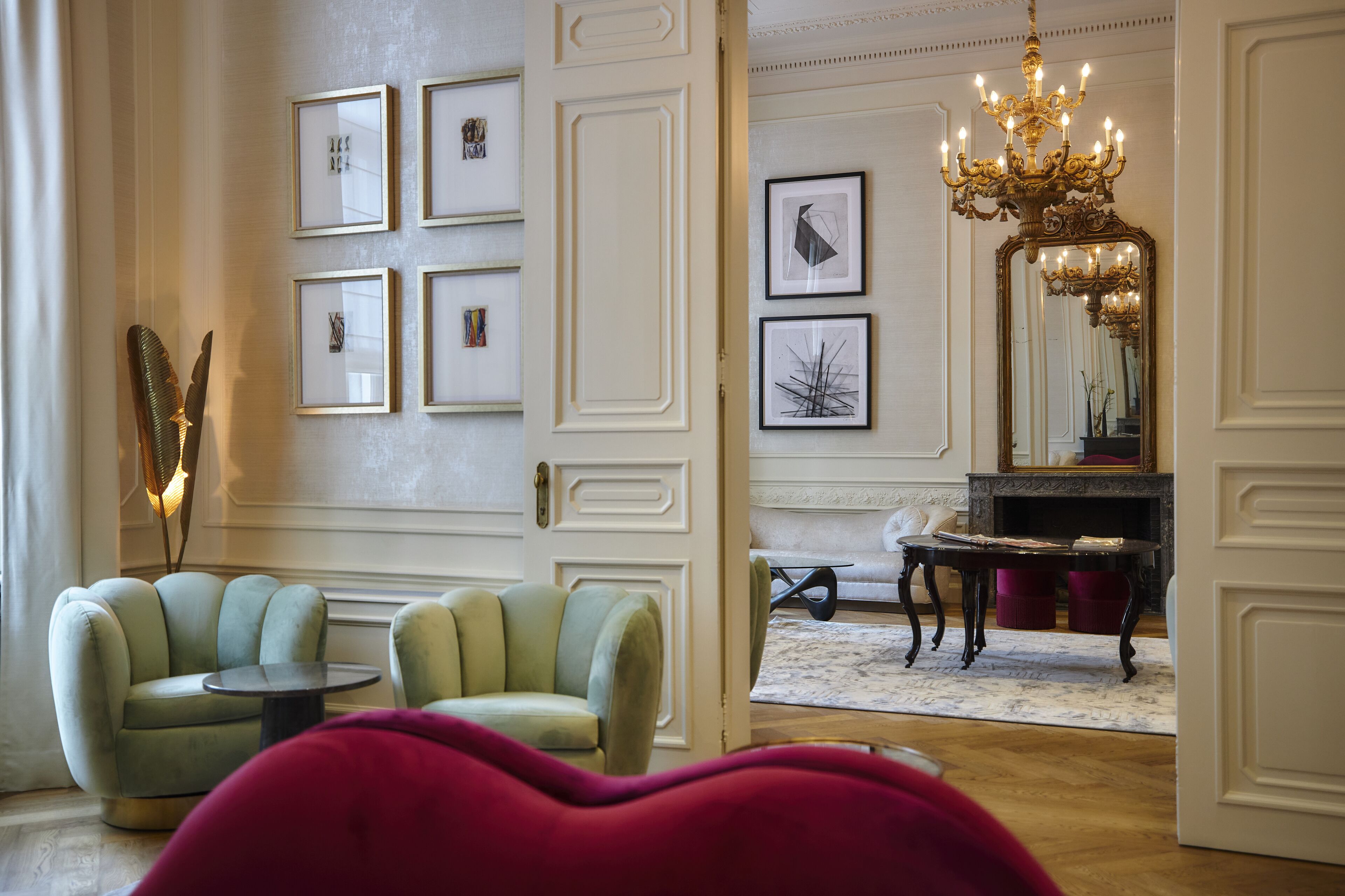 Une pièce dotée d’un lustre, de tableaux encadrés accrochés au mur, d’une cheminée et de deux fauteuils verts.