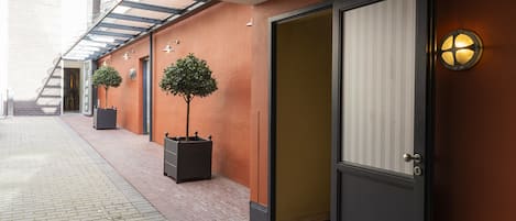 A corridor with a glass door, potted plants, and a wall-mounted light fixture.