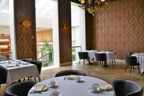 A dining area with round tables set for service, large windows, and a patterned wall. - Dukes’ Arches – by Dukes’ Hotel Collection (Bruges)