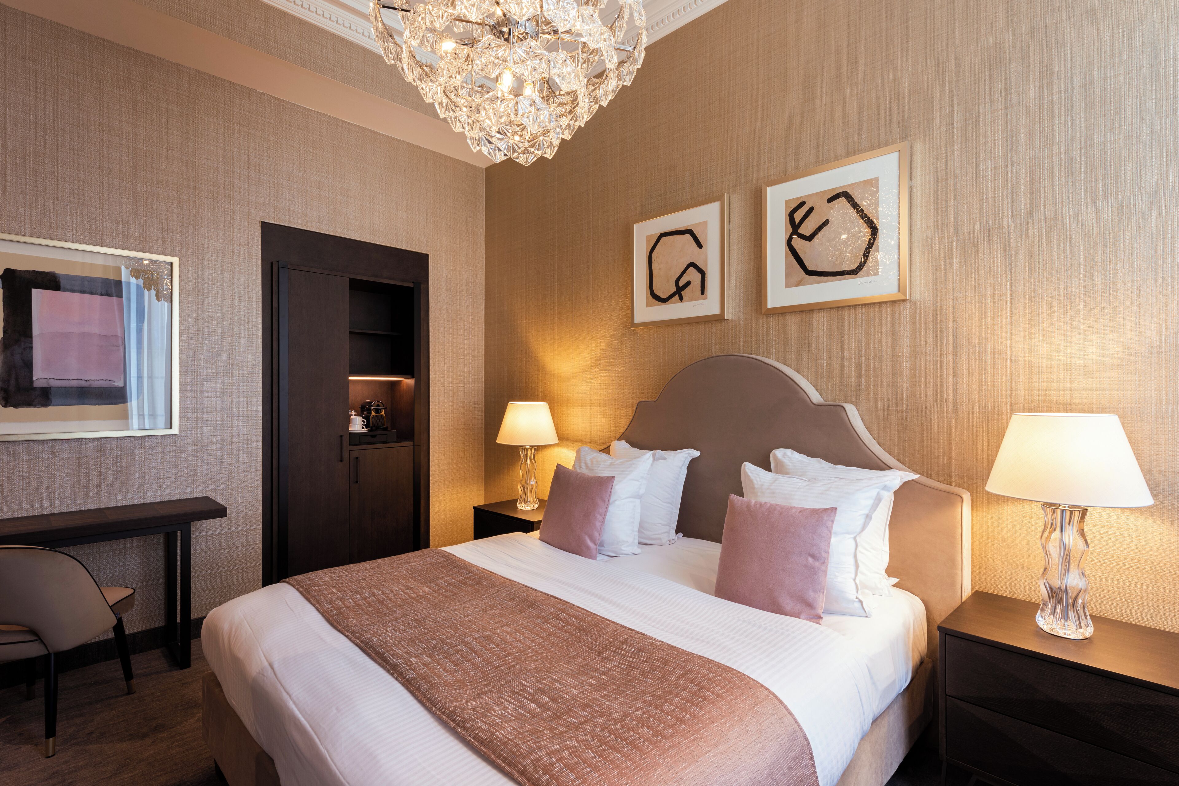 Une chambre d’hôtel avec un grand lit, des lampes de chevet, un bureau et un lustre.