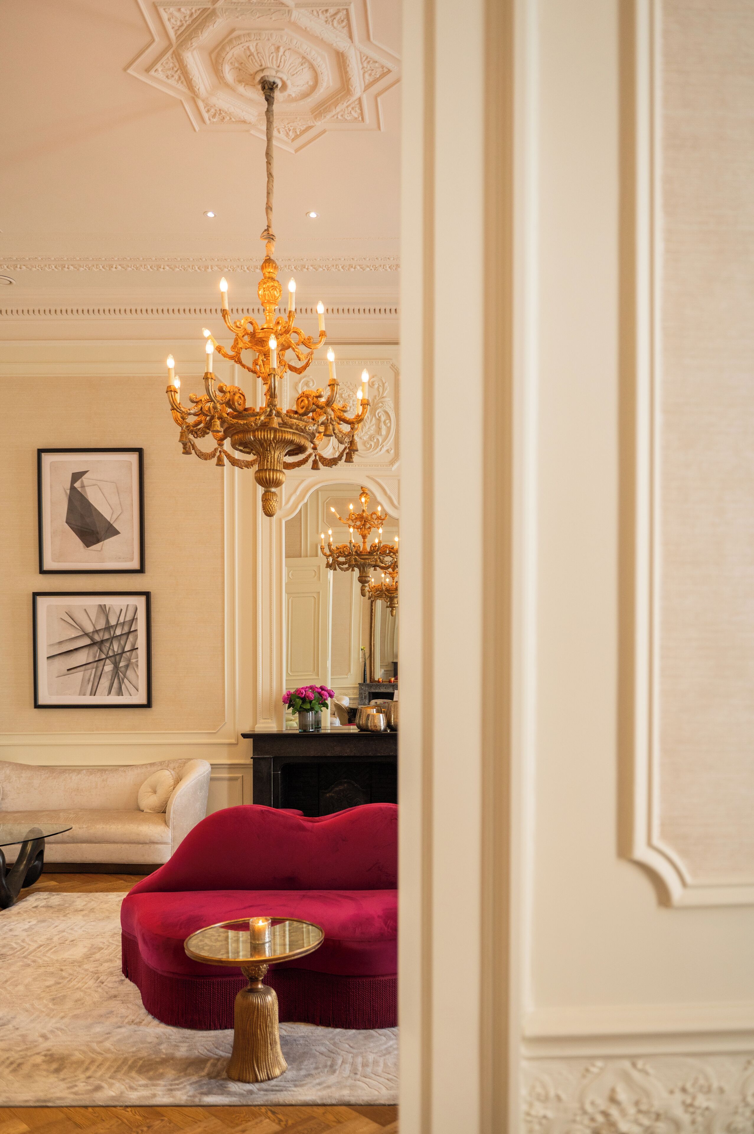 A room with a chandelier, a red sofa, and a round table.