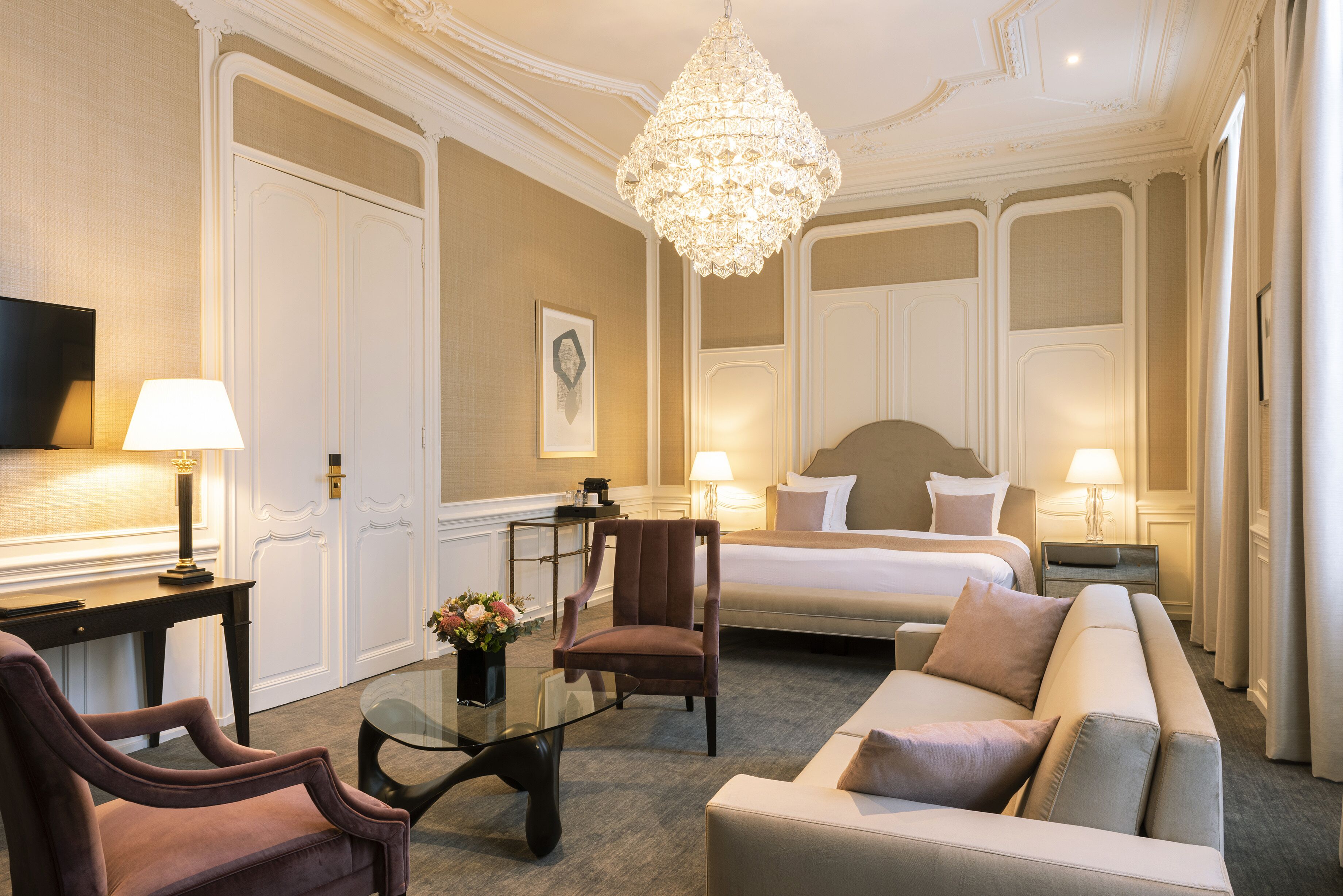 Une chambre d’hôtel avec un grand lit, un canapé, un fauteuil, un bureau et un lustre.