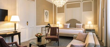Une chambre d’hôtel avec un grand lit, un canapé, un fauteuil, un bureau et un lustre.