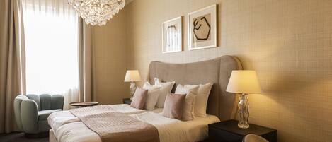 A hotel room with a large bed, two bedside tables with lamps, a decorative chandelier, and two framed pictures on the wall.