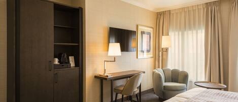 A hotel room with a bed, a desk, a chair, a wardrobe, and a small table.