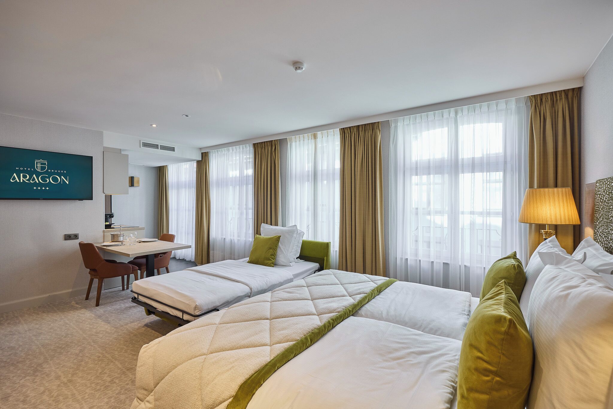 A hotel room with two beds, a desk, and a television.
