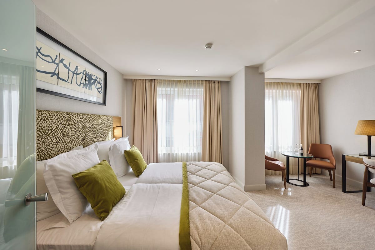 A hotel room with a large bed, two chairs, a small table, and a lamp.