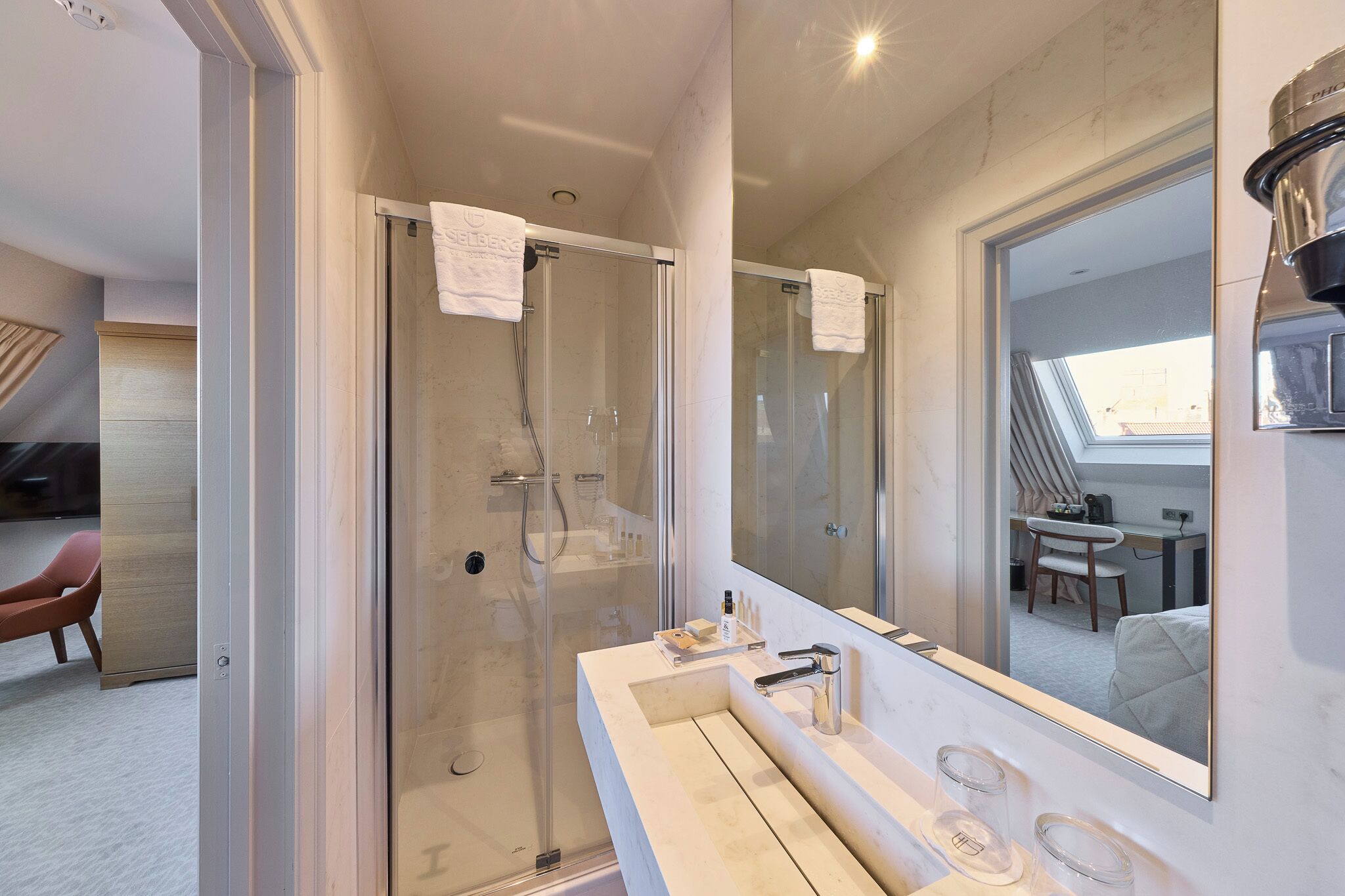 A modern bathroom with a glass shower enclosure, a large mirror, and a vanity with a sink and two faucets.