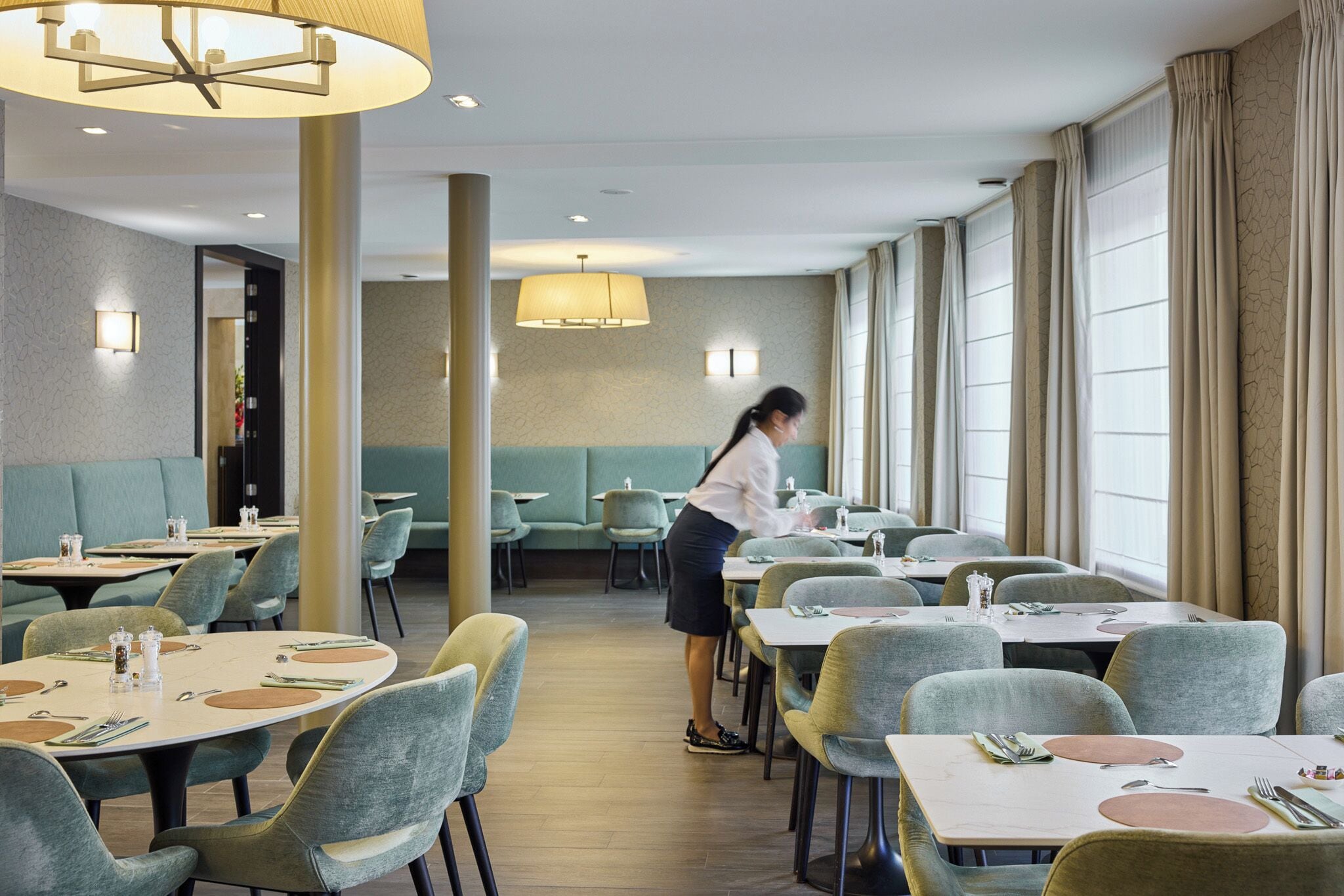 A restaurant with round tables, green upholstered booths, and a waitress.