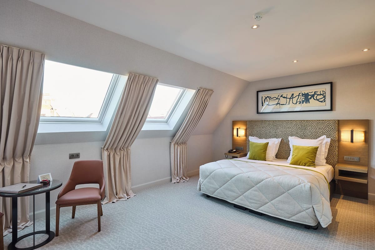 A hotel room with a bed, a desk, a chair, and a window with curtains.