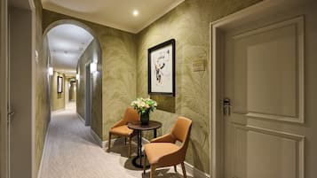 A hallway with a carpeted floor, a round table with chairs, a vase with flowers, and a framed artwork on the wall.