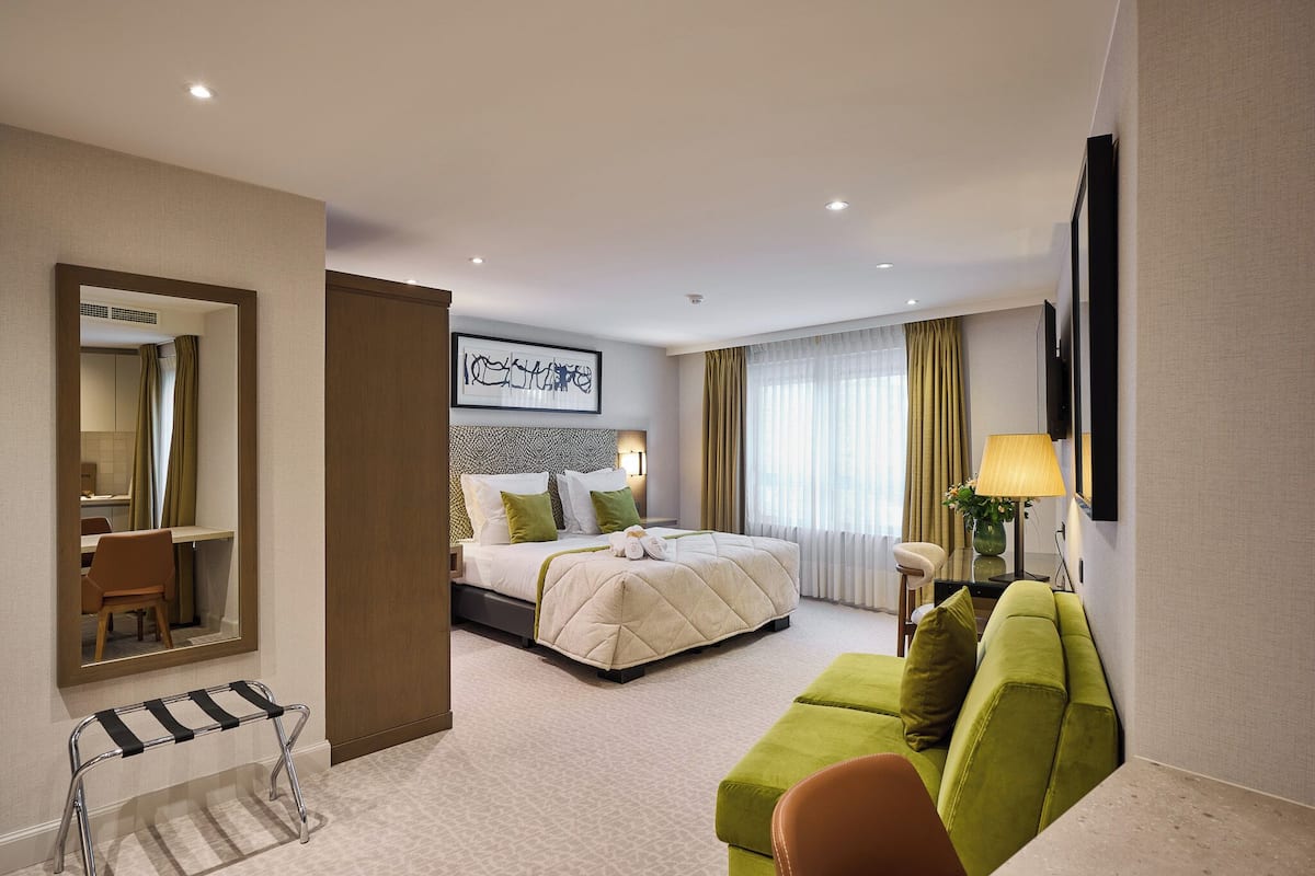 A hotel room with a bed, a green sofa, a desk, and a mirror.
