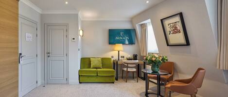 A hotel room with a green sofa, a small table with a lamp, a framed picture on the wall, and a bed in the foreground.