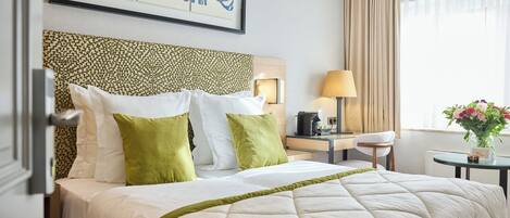 Une chambre d’hôtel avec un lit, un bureau avec une lampe, une chaise et une fenêtre avec des rideaux.