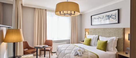 A hotel room with a bed, a desk, a chair, a lamp, and a painting on the wall.