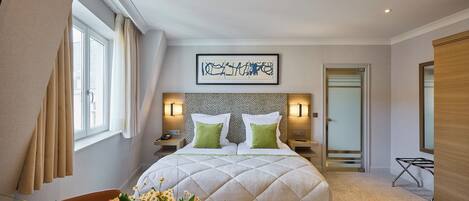 Habitación de hotel moderna con una cama grande, una mesita de noche, una lámpara y una obra de arte en la pared, además de un ventanal con cortinas.