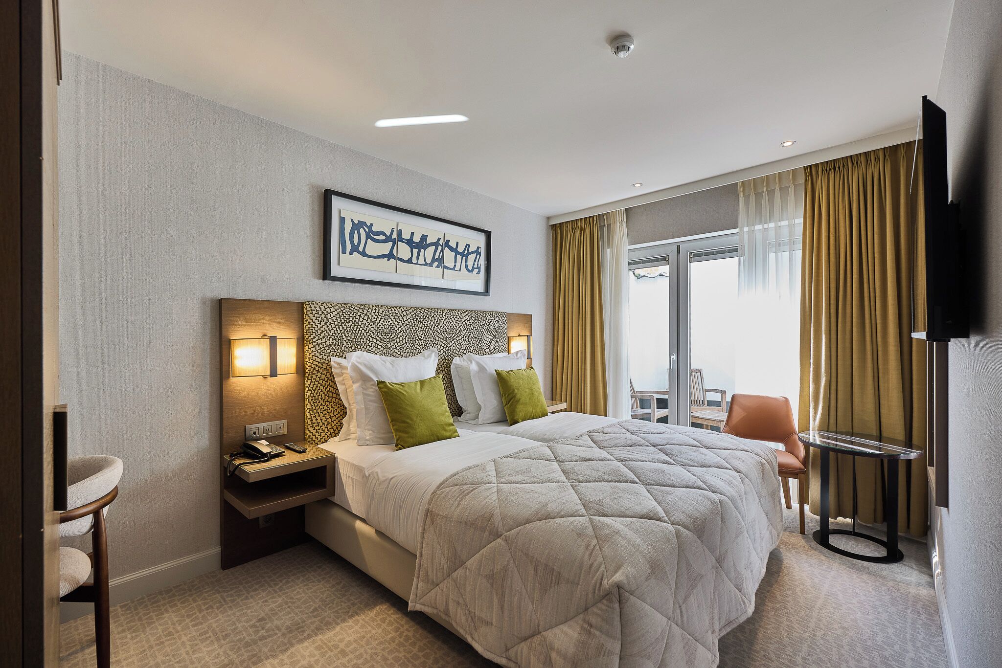 A hotel room with a large bed, a desk with a chair, a TV, and a window with curtains.