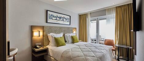 A hotel room with a large bed, a desk with a chair, a TV, and a window with curtains.