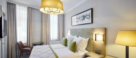 A hotel room with a large bed, a desk, a chair, a television, and a wall-mounted artwork.