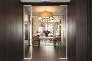 Un moderno vestíbulo de hotel con un separador de diseño geométrico, una mesa central con un jarrón de flores y una lámpara colgante grande.