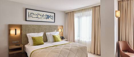 A hotel room with a large bed, a headboard with a patterned design, a bedside table with a lamp, and a chair.