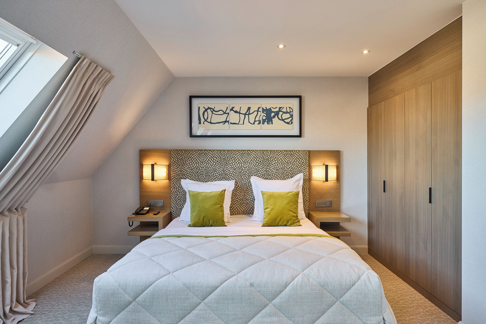 A hotel room with a large bed, a headboard with a patterned design, two bedside lamps, and a framed artwork on the wall.
