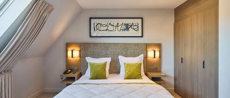 A hotel room with a large bed, a headboard with a patterned design, two bedside lamps, and a framed artwork on the wall.