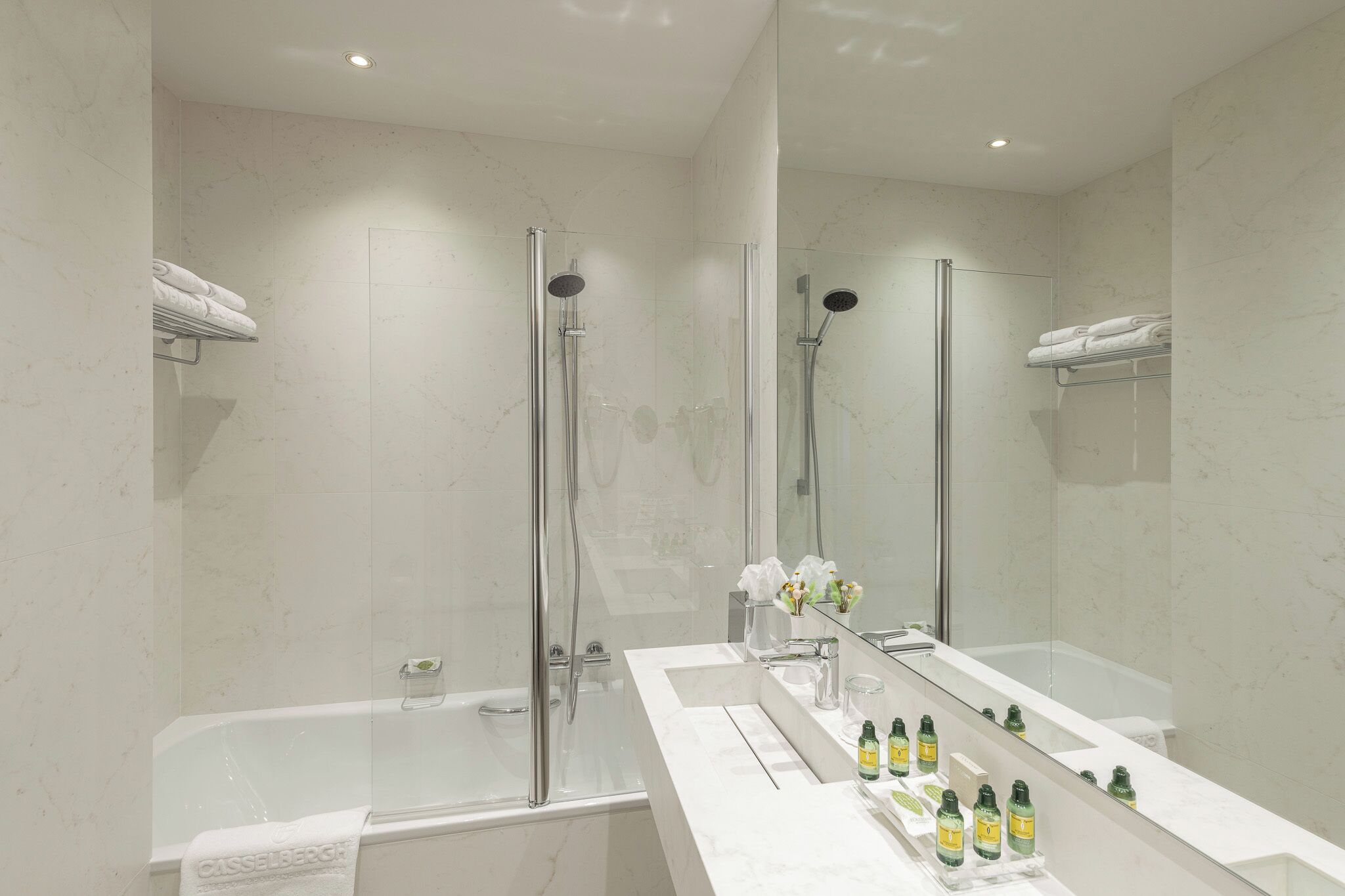 A modern bathroom with a glass-enclosed shower, a large mirror, and a vanity with toiletries.