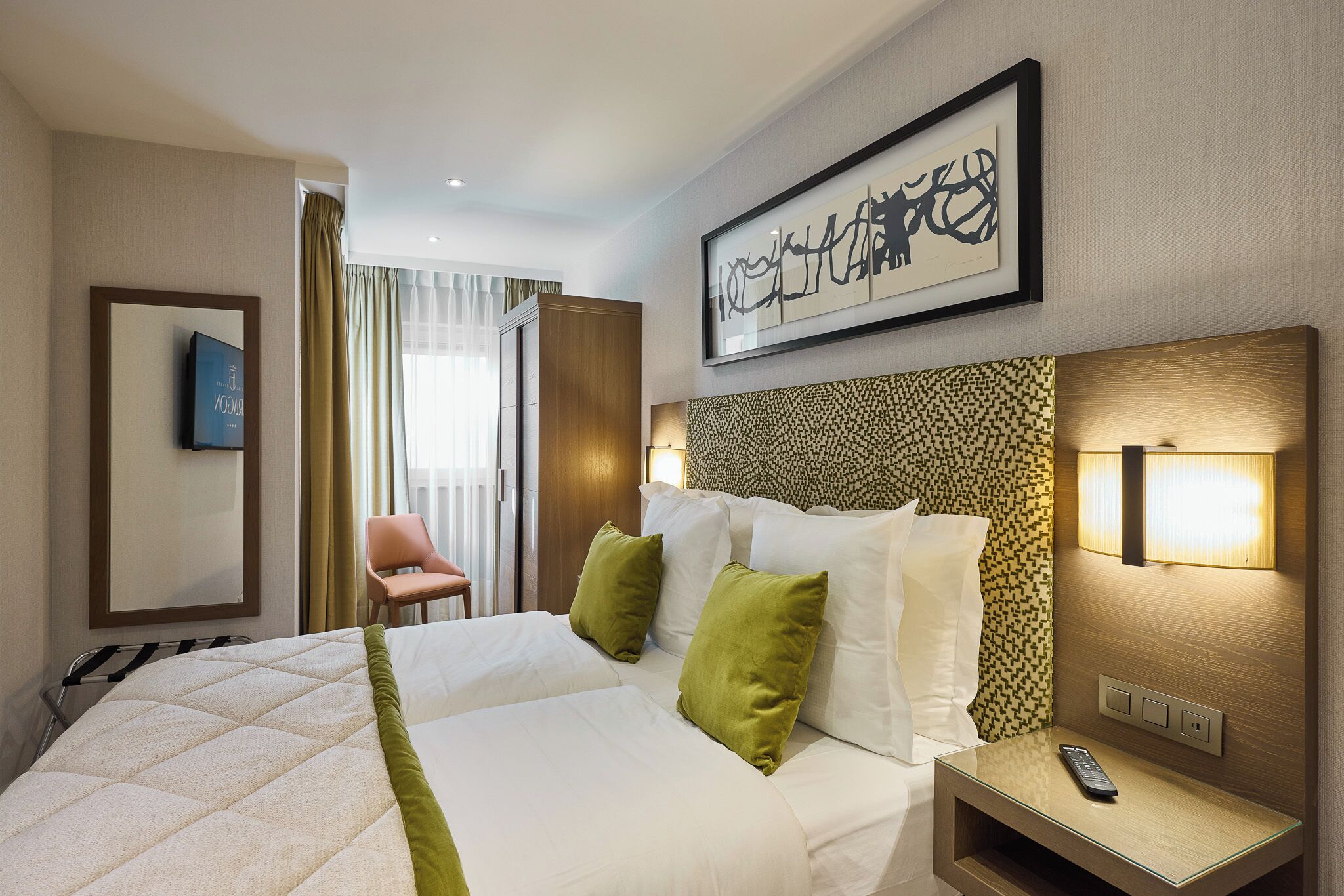Habitación de hotel con una cama grande, una mesita de noche con un control remoto, una silla y un televisor montado en la pared.