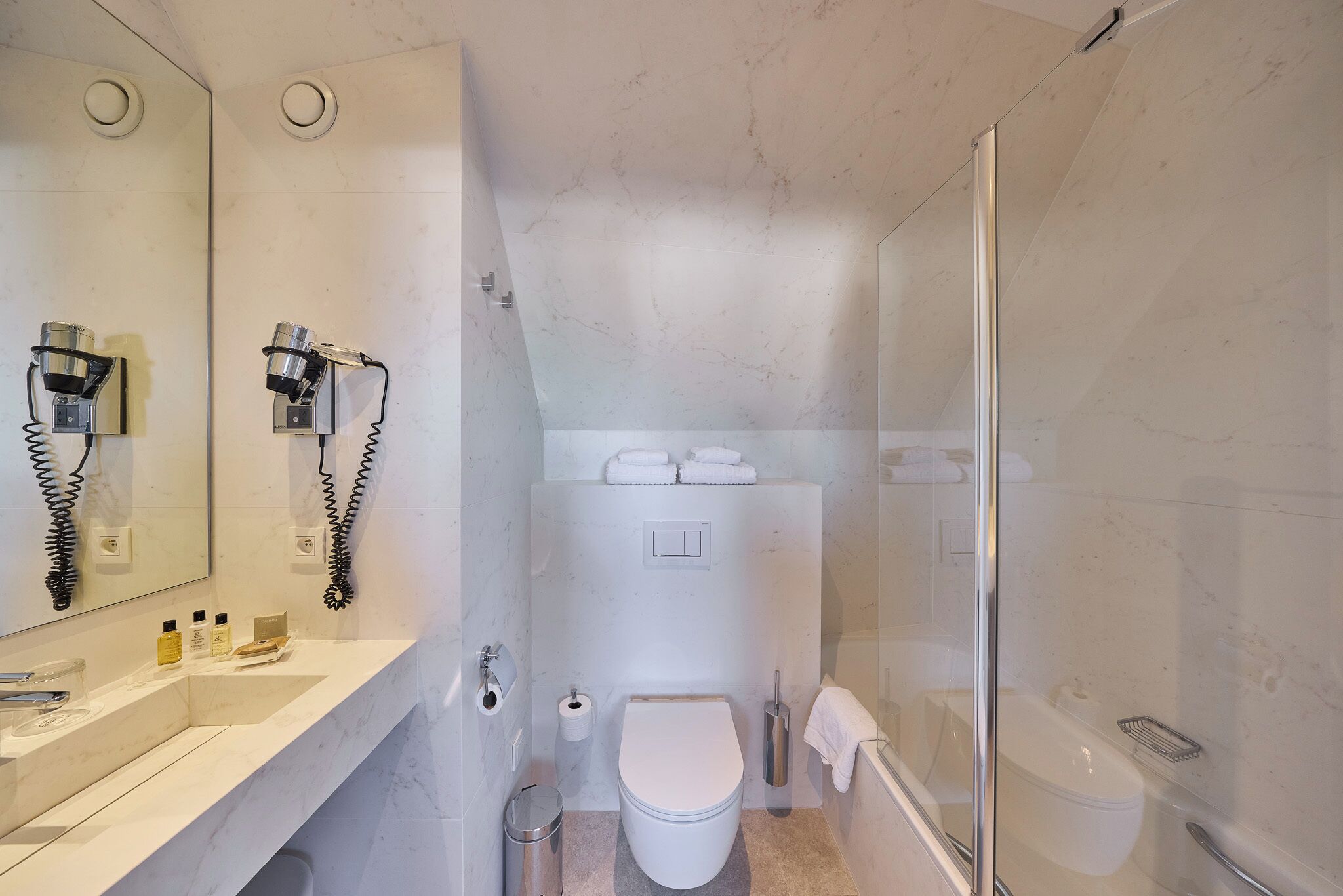 A modern bathroom with a marble sink, a toilet, and a glass-enclosed shower.