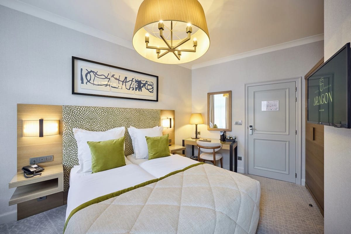 A hotel room with a large bed, bedside tables, a desk, a chair, a desk lamp, a mirror, and a television.