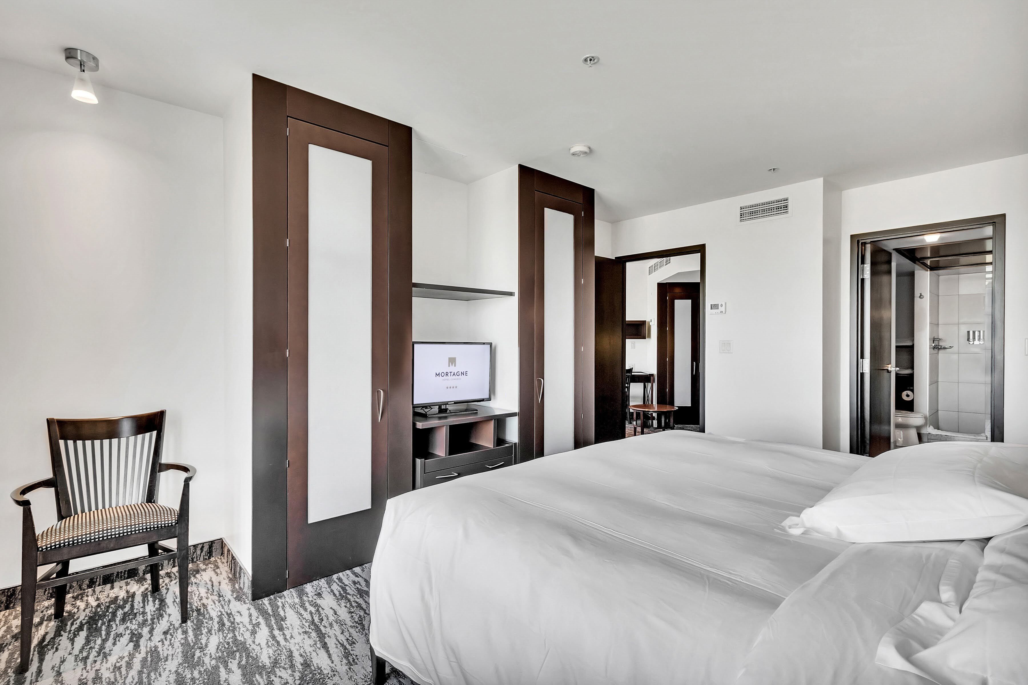 Une chambre d’hôtel avec un grand lit, une télévision, une chaise et une armoire.