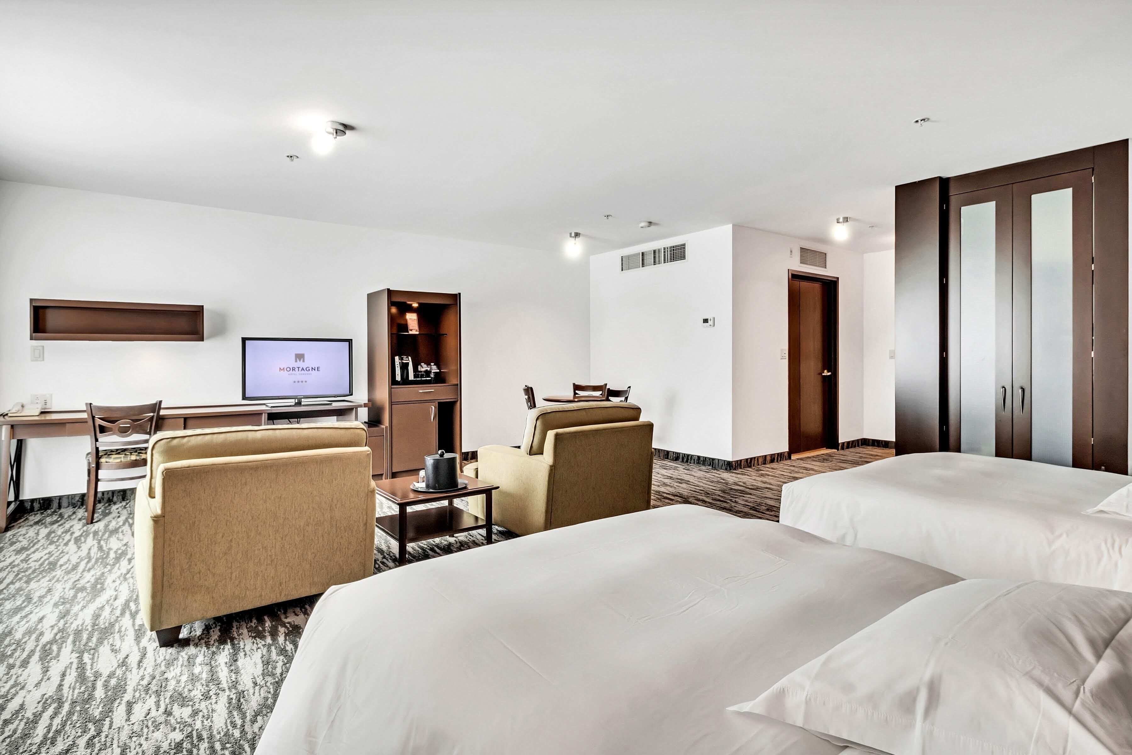 Une chambre d’hôtel avec deux lits, un bureau avec un ordinateur, une télévision, un minibar et une armoire.