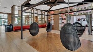 A modern interior with hanging chairs, a reception desk, and a bookshelf. - Hotel Mortagne (Boucherville)