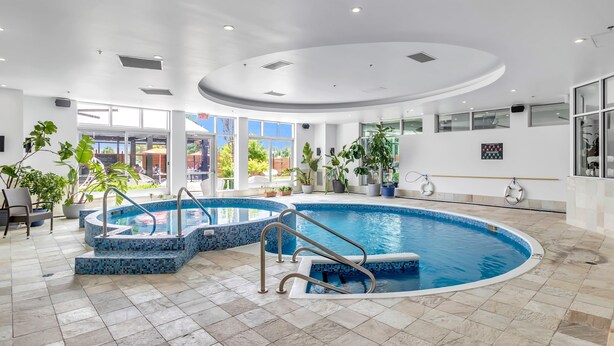 An indoor swimming pool with a tiled floor and a curved ceiling. - Hotel Mortagne (Boucherville)