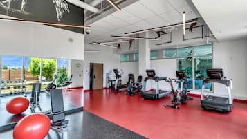 Uma academia com equipamentos de ginástica, janelas amplas e piso vermelho.