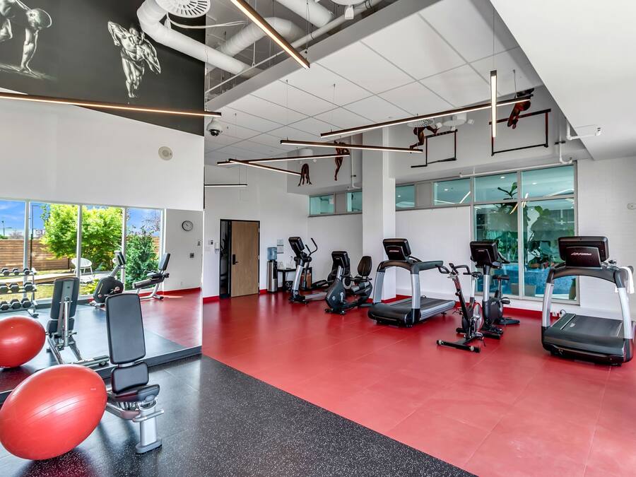 A gym with exercise equipment, large windows, and a red floor.