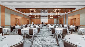 Une grande salle de conférence équipée de plusieurs tables rondes, de chaises et d’un écran de projection à l’avant.
