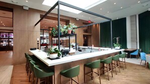 A modern bar area with a high ceiling, wooden flooring, and green bar stools. - Hotel Mortagne (Boucherville)