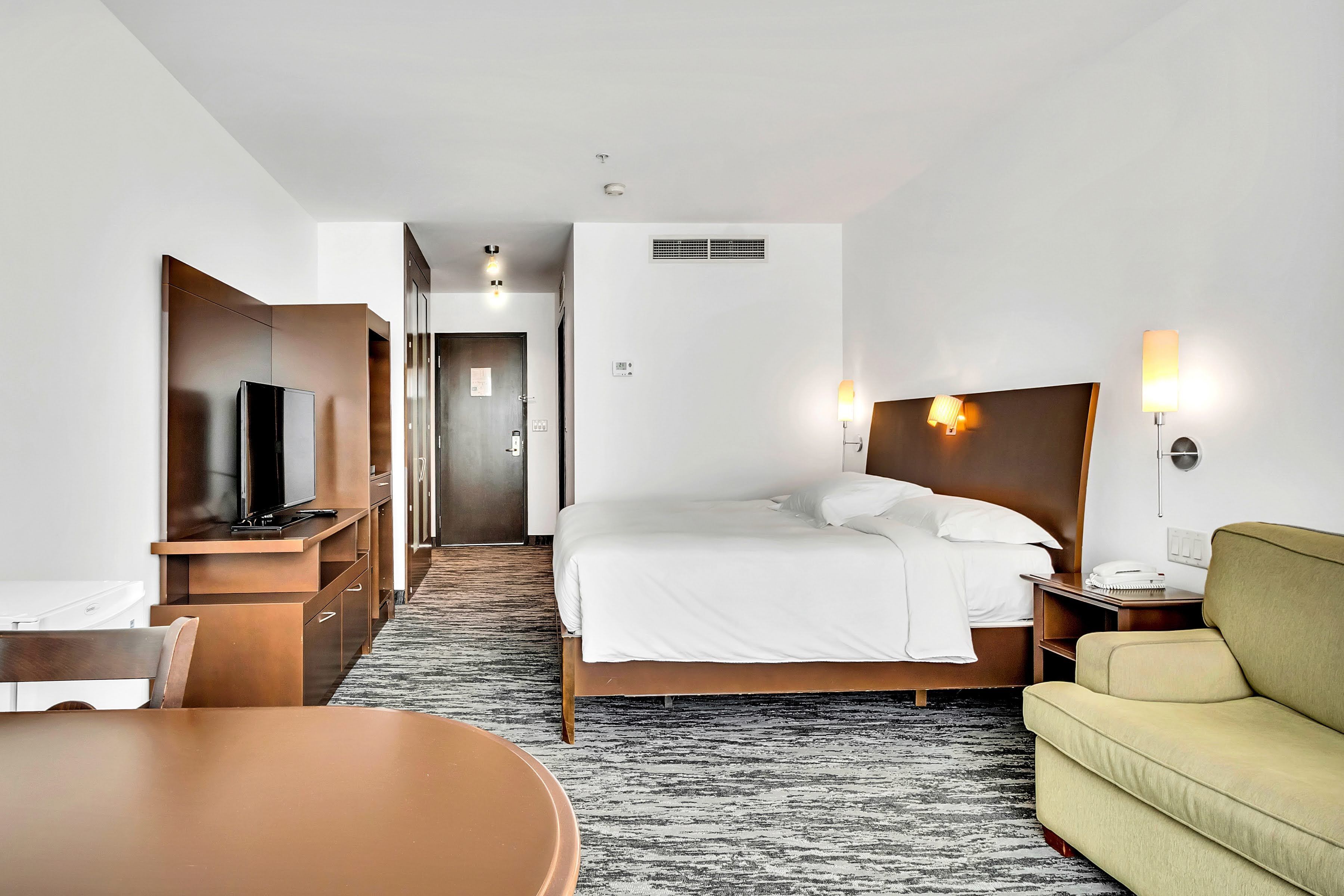 Camera d'albergo con un letto, comodino, lampada, televisore e un'area pranzo con tavolo e sedie.