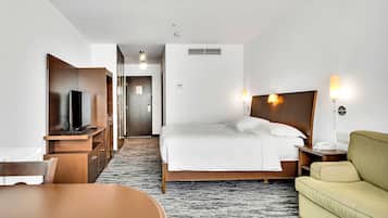 Camera d'albergo con un letto, comodino, lampada, televisore e un'area pranzo con tavolo e sedie.