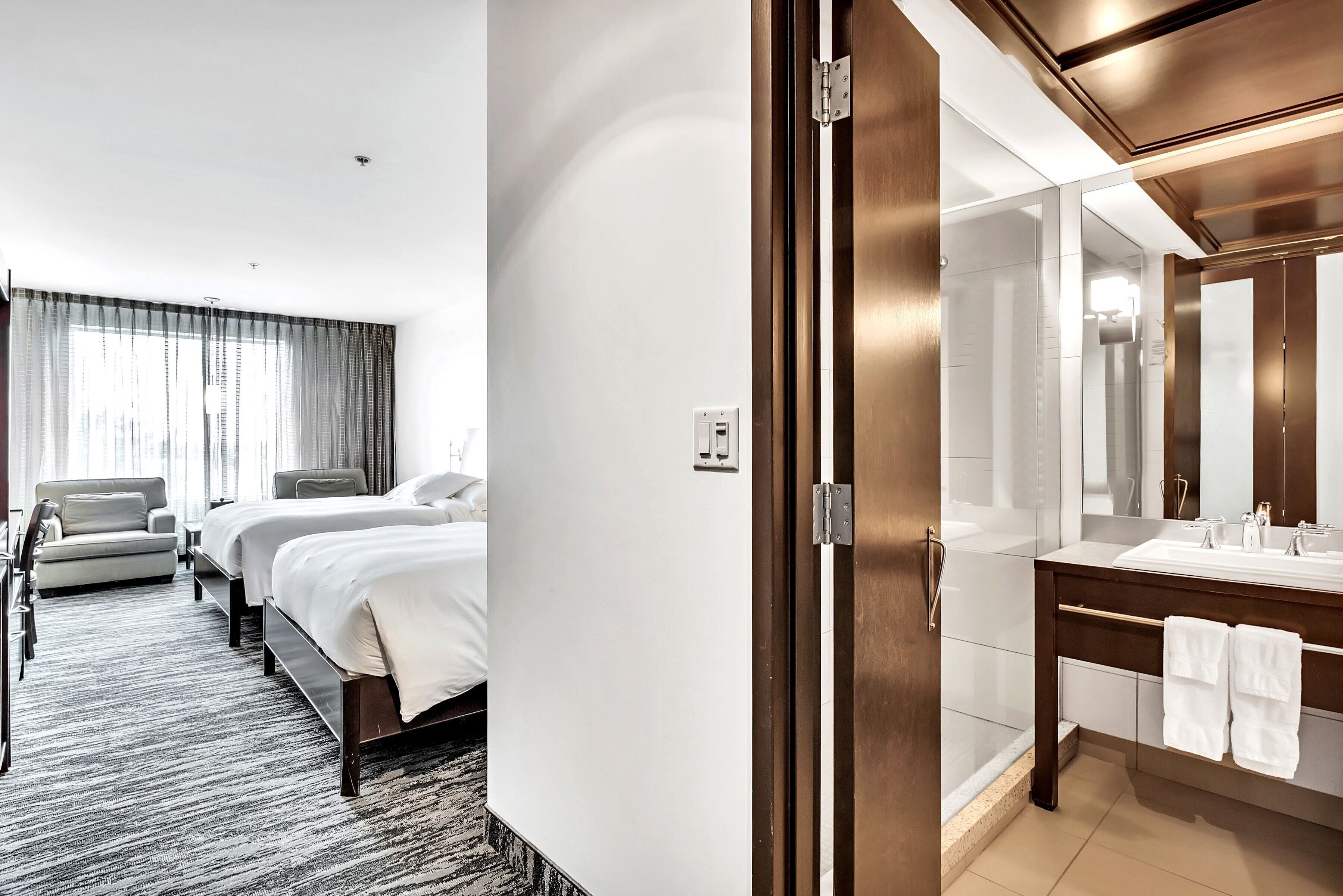 Ein Hotelzimmer mit Bett, einer Sitzecke, einem Badezimmer inklusive Spiegel und Dusche.