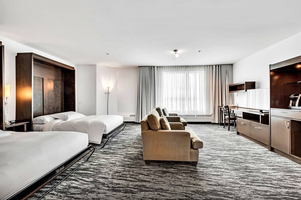 A hotel room with two beds, a sofa, a desk, and a TV.