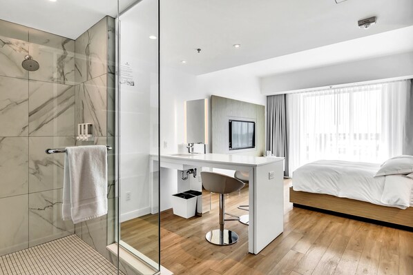 Una habitación de hotel moderna con ducha, escritorio, cama y un ventanal grande.