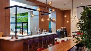 A modern bar area with a long wooden counter, bar stools, and a seating area with a large wooden table. - Hotel Mortagne (Boucherville)