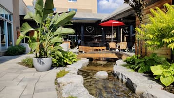 A courtyard with a small water feature, potted plants, outdoor seating, and a red umbrella.