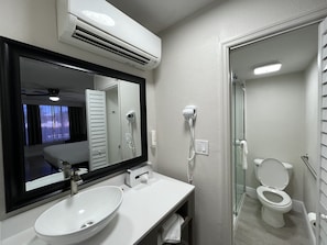A modern bathroom with a large mirror, white sink, and a glass shower enclosure.