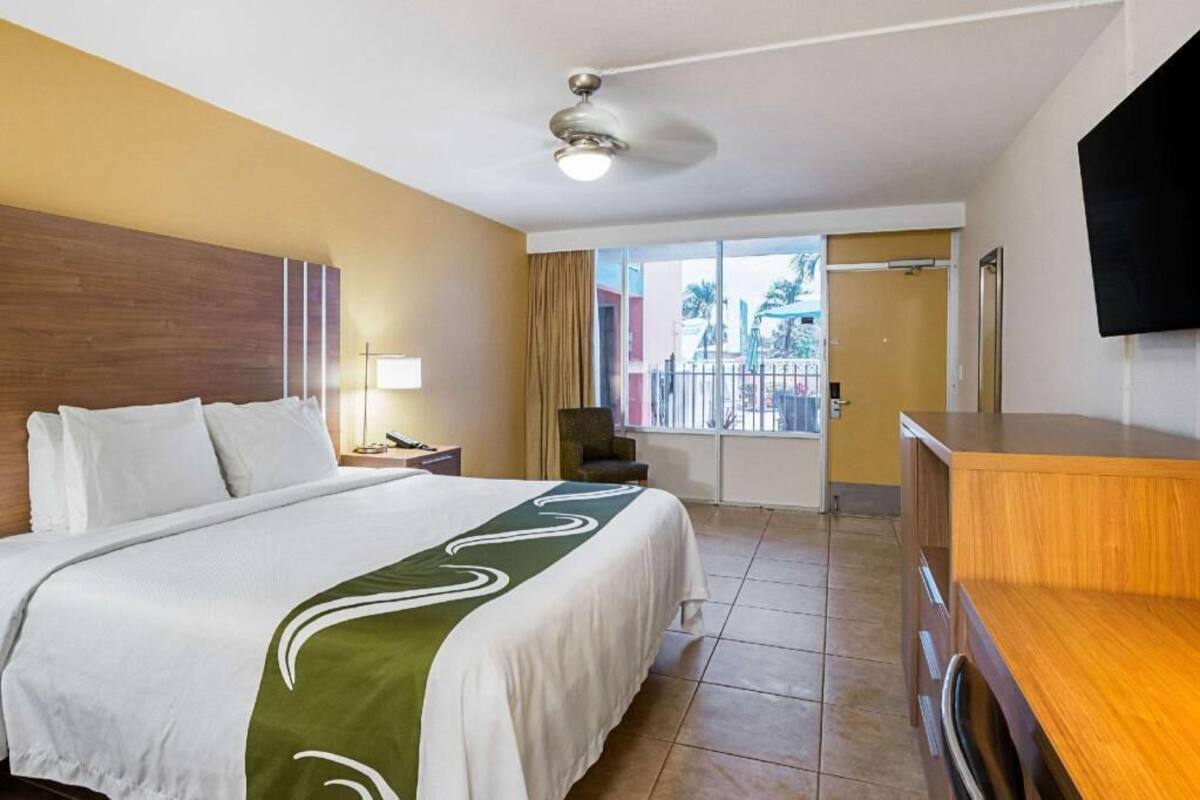 Een hotelkamer met een bed, een bureau, een stoel, een televisie en een balkon met uitzicht.